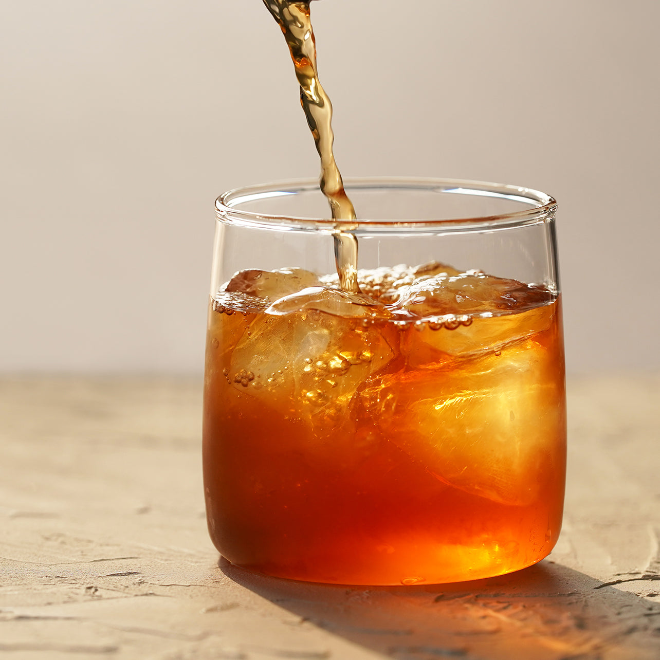 Nakamura Tokichi Hojicha roasted green tea being poured over ice in a glass cup.
