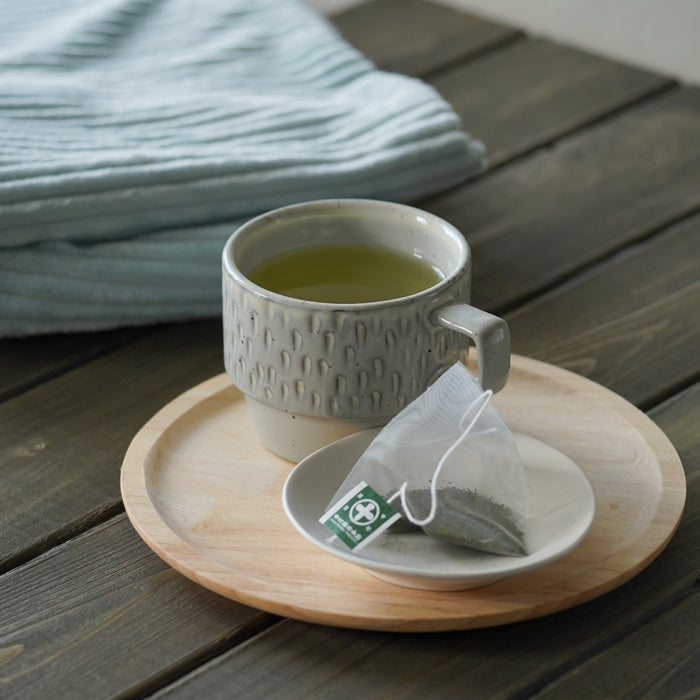 Nakamura Tokichi Sencha Tea Bag brewed a clear golden green tea, served in a modern ceramic cup on a minimalist wooden plate for a calm and relaxing home tea experience.