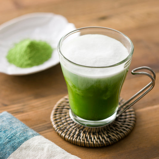 A warm glass cup of Nakamura Tokichi Sweetened Green Tea with a small plate of premium Matcha mix powder in the background