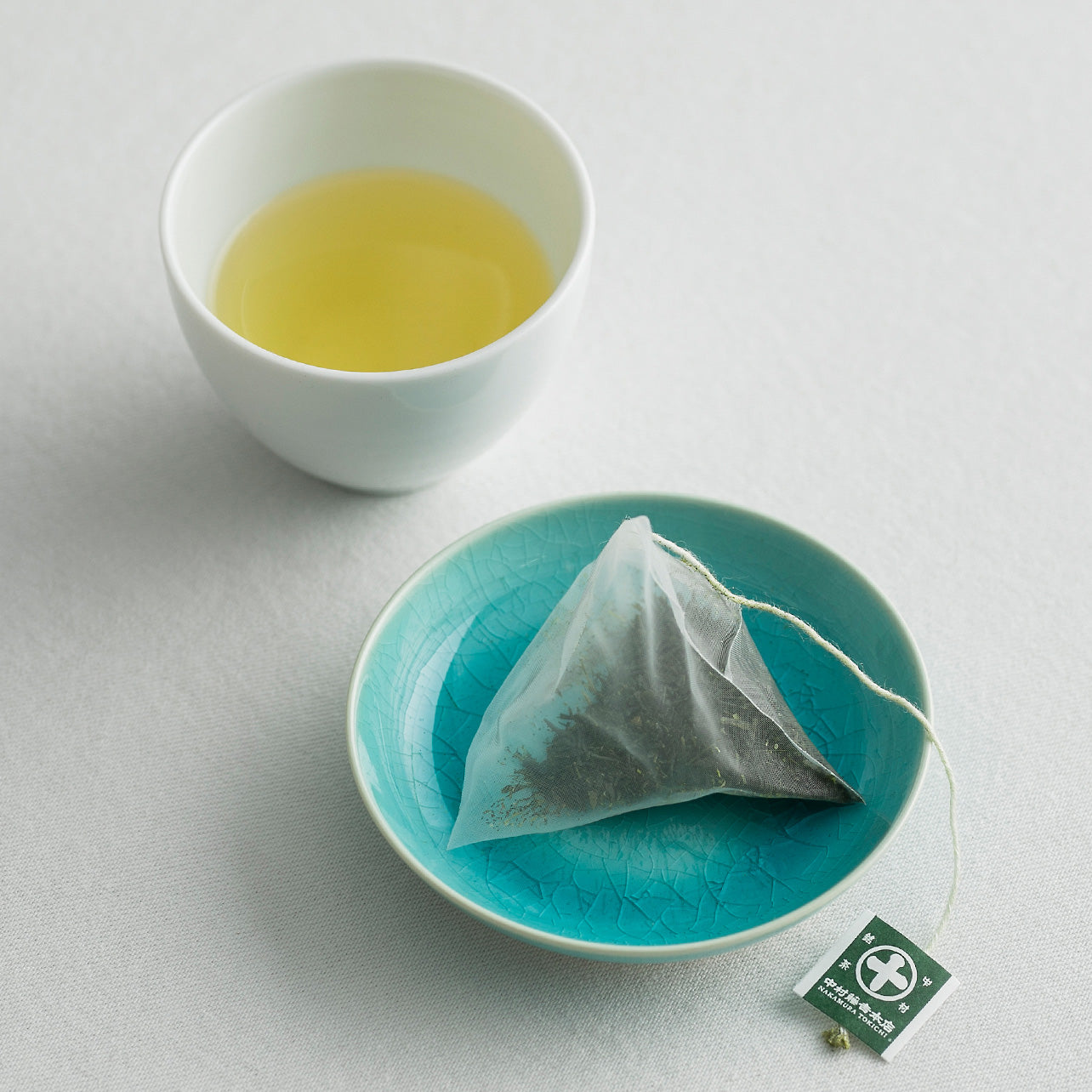 Nakamura Tokichi Sencha Tea Bag on a plate with green tea being poured into a cup.