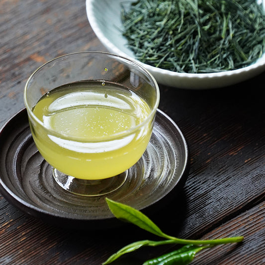 Nakamura Tokichi Uji First Tea of the season poured into a grass cup, displayed with leaf tea on a plate.